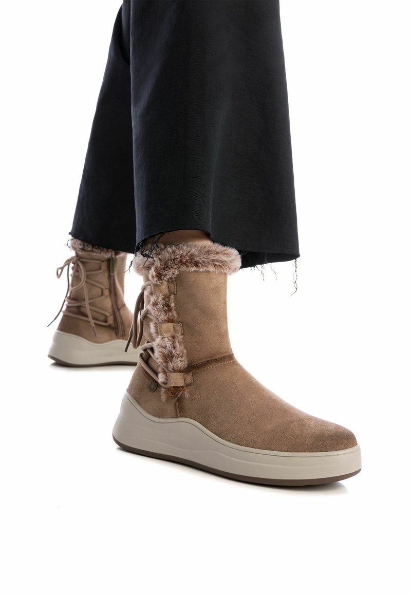 Botas de ante marrón con forro de piel sintética, diseño de cordones y suela de goma gruesa de color claro. Combinadas con pantalones negros recortados.