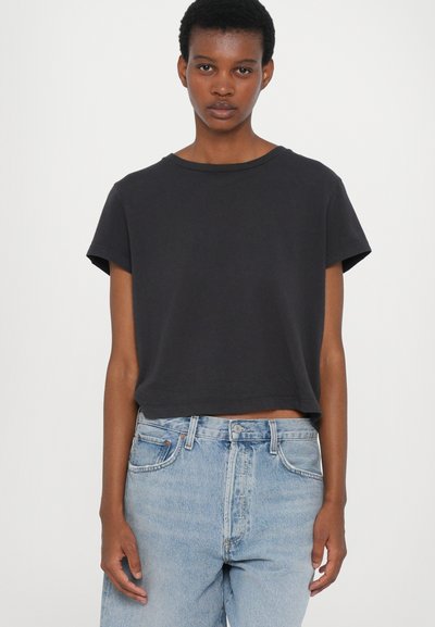 T-shirt noir court en coton doux, avec des manches courtes et un col rond, associé à un jean taille haute bleu clair.