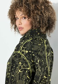 Sudadera de punto con un patrón abstracto en negro y amarillo, cuello alto y detalles de costura en contraste. Tela texturizada con un corte relajado.