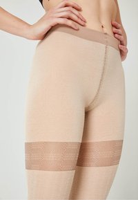 Leggings beige con una finitura testurizzata, cintura liscia e dettagli a motivo in una tonalità più scura vicino al polpaccio.