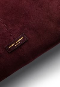 Burgundy suede clutch bag featuring a textured leather label with "ISABEL BERNARD" and "PARIS" in gold lettering.
