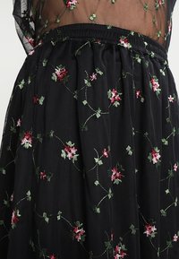 Zwarte rok met een elastische tailleband, voorzien van intricaat bloemenborduurwerk in rood en groen, met een doorschijnende textuur en een verfijnd ontwerp.