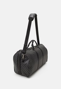 Sac de voyage à carreaux noirs en matériau texturé. Il dispose de poignées doubles et d'une bandoulière amovible avec des zips et des accessoires en métal argenté.