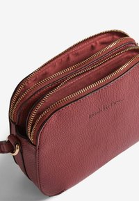 Borsa a tracolla in pelle testurizzata color bordeaux con due zip dorate aperte e testo in rilievo "amici come questi..." sul davanti.
