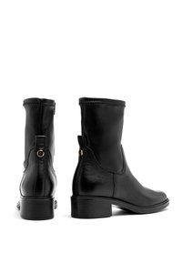 Bottines en cuir noir avec une finition texturée, bout arrondi et petit talon carré. Montées avec des éléments métalliques dorés sur le côté.