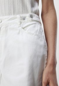 Witte denimbroek met een voorke pocket, twee metalen knopen in de taille en een gladde textuur, met subtiele stikdetails.