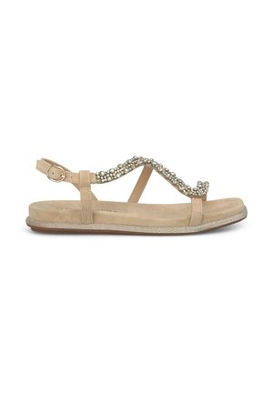 Sandalia beige con suela plana, que presenta una onda decorativa de piedras preciosas transparentes en la correa y una hebilla ajustable en el tobillo.