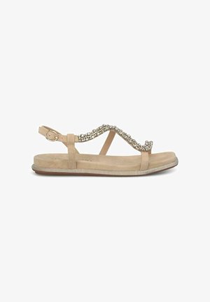Sandalia beige con suela plana, que presenta una onda decorativa de piedras preciosas transparentes en la correa y una hebilla ajustable en el tobillo.