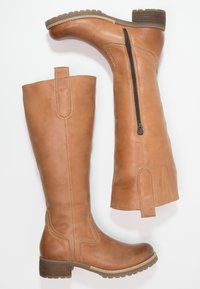 Bottes en cuir marron hautes avec une fermeture éclair sur le côté, un talon renforcé et une semelle texturée. Comprend des coutures et une languette pour un enfilage facile.