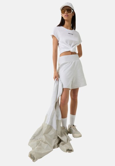 White cropped t-shirt with logo, light gray shorts, gray jacket, and beige sneakers. Accessories include white socks and a cap with sunglasses.