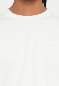 Λευκό βαμβακερό μπλουζάκι με στρογγυλή λαιμόκοψη. Διαθέτει διακριτικό τονικό λογότυπο στο στήθος και λεία υφή. Απλός και ευέλικτος σχεδιασμός.