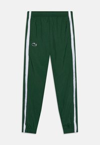 Pantaloni sportivi verde scuro con strisce laterali bianche, vita elastica, polsini alla caviglia e un piccolo logo di coccodrillo sulla coscia sinistra.