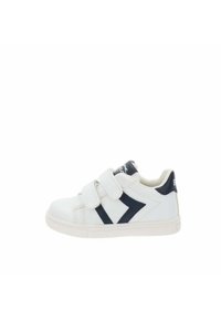 Baskets blanches pour enfants avec un motif de flèche noire, deux bandes auto-agrippantes et une semelle en caoutchouc sur fond blanc.