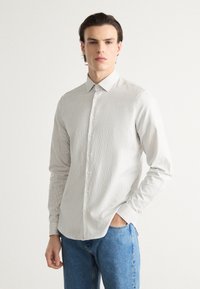 Langärmliges Hemd mit Knöpfen in Hellgrau mit einem subtilen Streifenmuster, aus strukturiertem Stoff, kombiniert mit blauen Jeans.