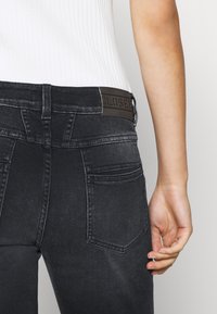 Jeans in denim nero con vestibilità slim, dotati di tasche posteriori e una toppa in pelle marrone sul elastico in vita. Tessuto testurizzato e design semplice.