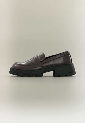 Tumepruun nahast loafers paksu musta massiivse tallaga ja madala plokk-kontsaga neutraalsel taustal.