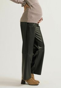 Hoch taillierte schwarze Kunstlederhosen mit weitem Bein. Kombiniert mit einem gerippten beigen Pullover und beigen Stiefeln mit Absatz. Glatte Textur, minimale Nähte.