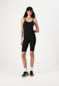 Un haut sans manches noir et un short de cyclisme, fabriqués en tissu lisse. Présente des bretelles fines et une coupe ajustée. Assorti avec des baskets noires et une casquette.