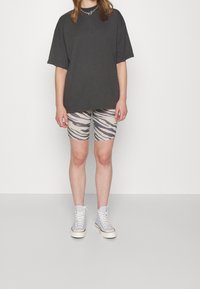 Persona vistiendo una camiseta negra oversized, pantalones cortos biker de estampado de cebra en beige y gris, zapatillas blancas de caña alta y un collar de cadena plateada.