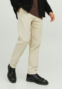 Pantaloni in velluto a coste beige con vestibilità dritta, caratterizzati da righe verticali e tasche laterali, abbinati a stivali neri con lacci.