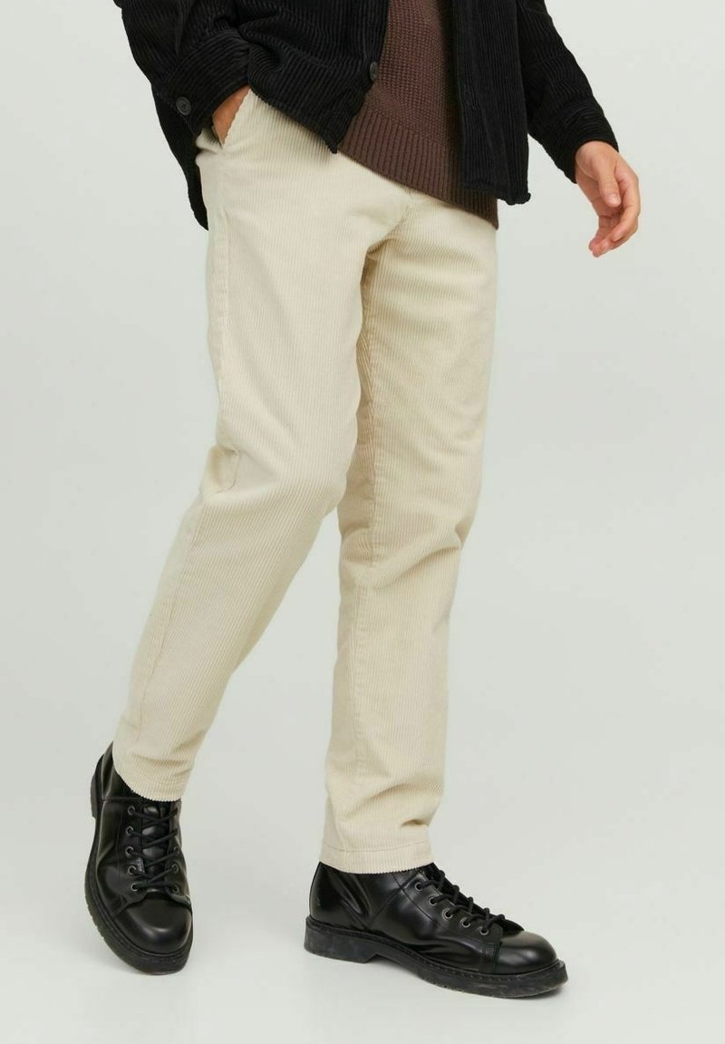 Pantaloni in velluto a coste beige con vestibilità dritta, caratterizzati da righe verticali e tasche laterali, abbinati a stivali neri con lacci.