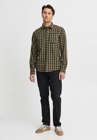 Cămașă cu carouri maro și neagră, cu un buzunar, asortată cu pantaloni negri și adidași gri cu dungi albe.