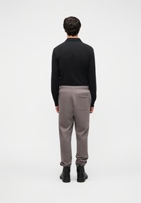 Μπλούζα μακρυμάνικη μαύρη με γιακά και μανσέτες με κουμπιά, σε συνδυασμό με γκρι παντελόνι jogger με πίσω τσέπη και μαύρα μποτάκια αστραγάλου.