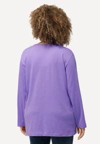 Langärmliges lila T-Shirt mit lockerer Passform, rundem Halsausschnitt und weicher Stoffqualität. Der Saum ist hinten leicht verlängert und zeichnet sich durch eine glatte Textur aus.