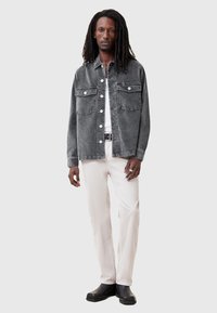 Chaqueta de denim gris con dos bolsillos en el pecho, botones blancos, usada sobre una camiseta blanca y pantalones beiges, combinada con botas negras.