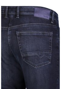 Dunkelblaue Jeans mit einer Nahaufnahme der hinteren Tasche, sichtbaren Steppnähten und einem kleinen gewebten Etikett am Bund.