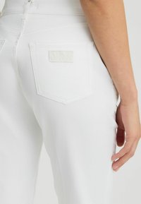 Pantalones de denim blanco con un diseño ajustado, que cuentan con bolsillos traseros y un parche de logo texturizado. Tejido suave con costuras limpias.