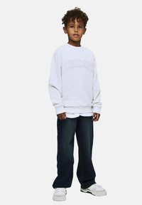 Sweatshirt gris avec "CHICAGO" brodé sur le devant, superposé à une chemise blanche et associé à un jean foncé et des baskets blanches.