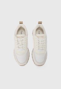 Sneaker in crema e beige con punta rotonda, parte superiore testurizzata, lacci e un tassello tan; con il marchio "Calvin Klein" sulla linguetta.
