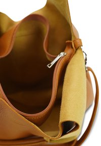 Bruine leren handtas met een suede binnenvoering. Voorzien van een ritsvak en een zachte textuur. De binnenkant heeft een zachte gele tint.