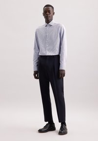 Camicia a scacchi blu chiaro con chiusura a bottoni, abbinata a pantaloni su misura scuri e scarpe stringate nere, il tutto su uno sfondo neutro.