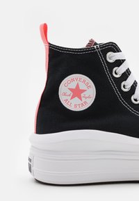 Baskets montantes Converse All Star noires avec semelle blanche, lacets blancs, écusson logo rose et languette au talon.