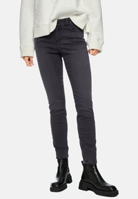 Schwarze, hoch taillierte Skinny-Jeans aus Denim mit glatter Textur und Kontrastnähten, kombiniert mit schwarzen Stiefeletten.
