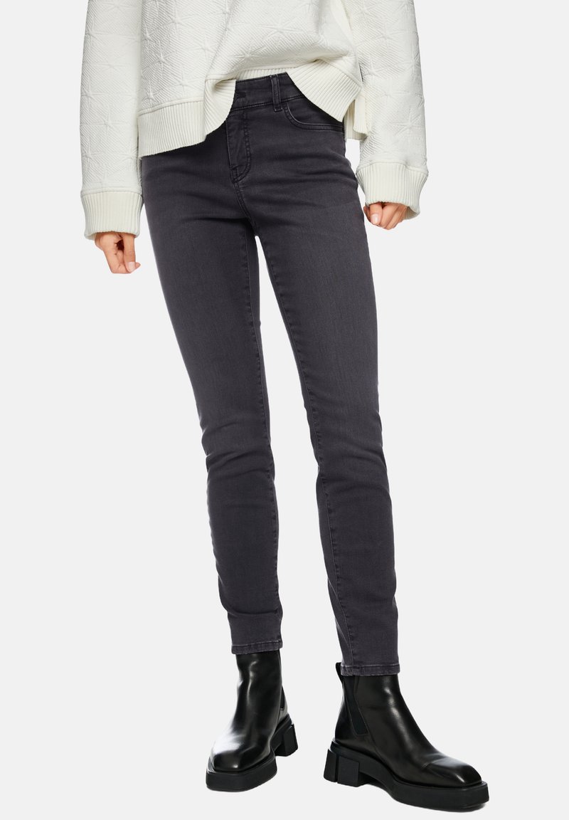 Schwarze, hoch taillierte Skinny-Jeans aus Denim mit glatter Textur und Kontrastnähten, kombiniert mit schwarzen Stiefeletten.
