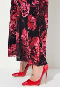 Červené lakované lodičky s špičatou špičkou. Černá sukně s velkým červeným květinovým vzorem. Hladká textura, délka do poloviny lýtek. Elegantní designové detaily.