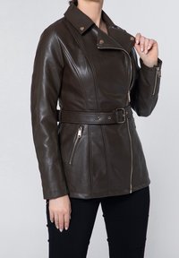 Giacca in pelle marrone con vita con cintura, tasche con cerniera e collo leggermente rialzato. Presenta un design aderente e una texture liscia.