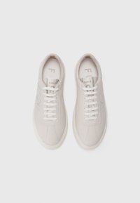 Sneaker bianche in pelle con una texture liscia, lacci beige a contrasto e dettagli del logo sottili sulla linguetta. Suola piatta in gomma.