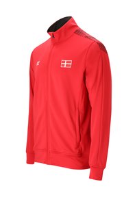 Röd sportjacka med hel dragkedja och hög krage, svart mönstrad axeldetalj, framfickor och ett vitt flaggemblem på bröstet.