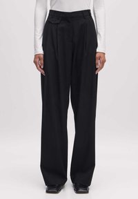 Zwarte geplooide broek met een hoge taille, gemaakt van een soepele stof. Beschikt over een schuine zak en een ontspannen, brede pasvorm.