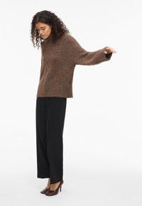 Pull en maille marron, confortable, à coupe décontractée et manches larges, assorti à un pantalon noir à coupe droite et des escarpins marron.