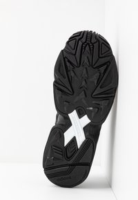 Svart atletisk sko sula med texturerad gummi, med ett vinklat mönster och en distinkt vit vridstångsdesign över mellanfoten.