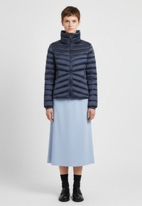 Marinblå puffjacka med hög krage, horisontell quiltning, framtida dragkedja och elastiska manschetter, ihop med en ljusblå midiklänning och svarta loafers.