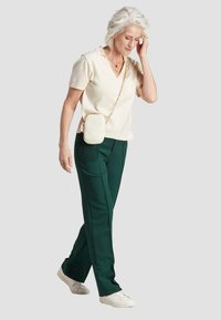 Polo shirt crème à manches courtes associé à un pantalon tailleur vert foncé et des baskets blanches. Un petit sac bandoulière blanc avec une chaîne en or.