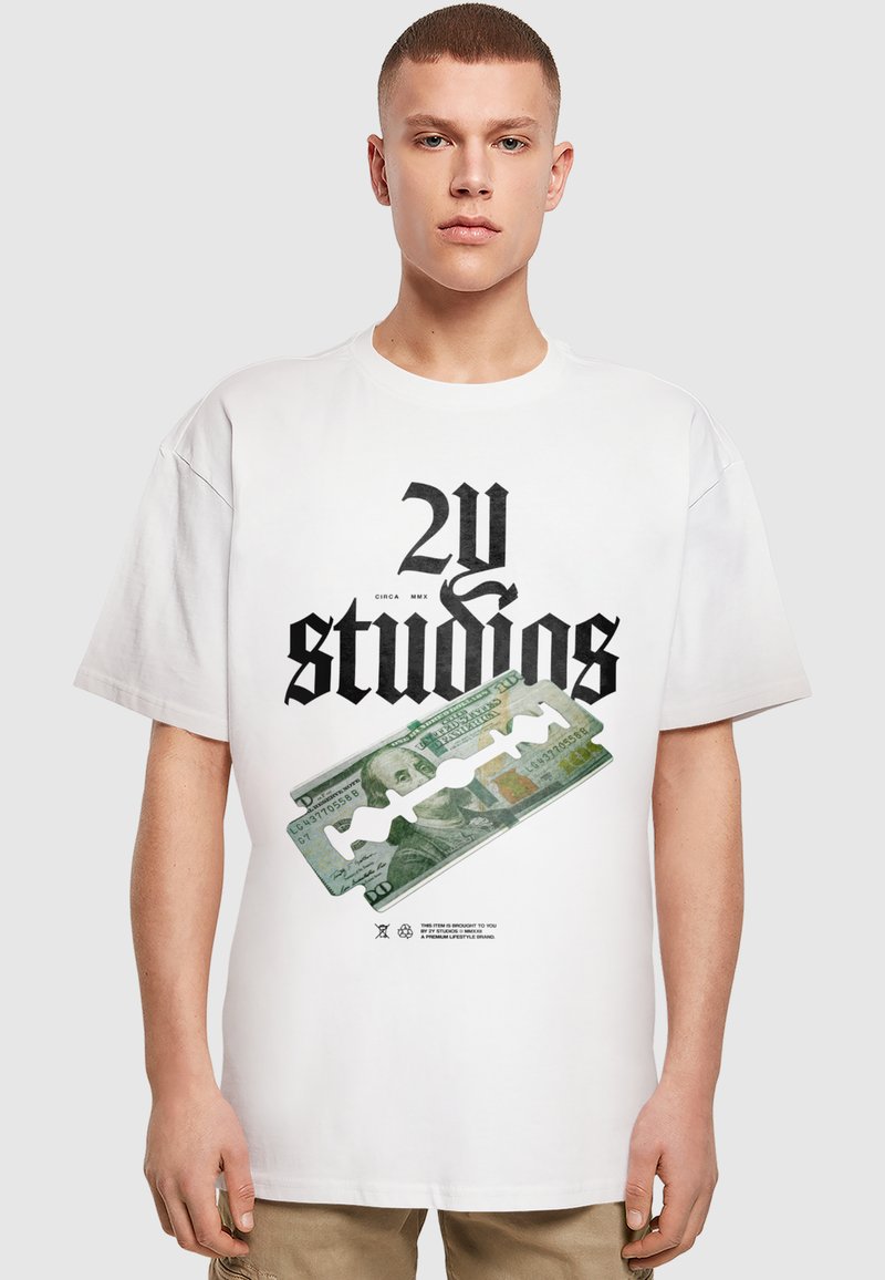 Balts pārdots t-krekliņš ar melnu grafisko tekstu "2Y studios" un zaļā dolāra rēķina attēlu, akcentēts ar skuvekļa asmeni.