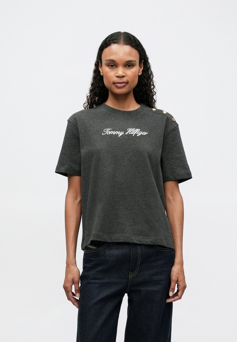 Dark gray cotton T-shirt with short sleeves, featuring a white "Tommy Hilfiger" logo, decorative gold buttons on the shoulder, and a relaxed fit.