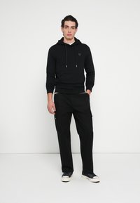 Schwarzer Kapuzenpullover mit Kängurutasche, Kordelzugkapuze und Logodetail. Kombiniert mit schwarzen Cargohosen mit Seitentaschen und lockerer Passform.